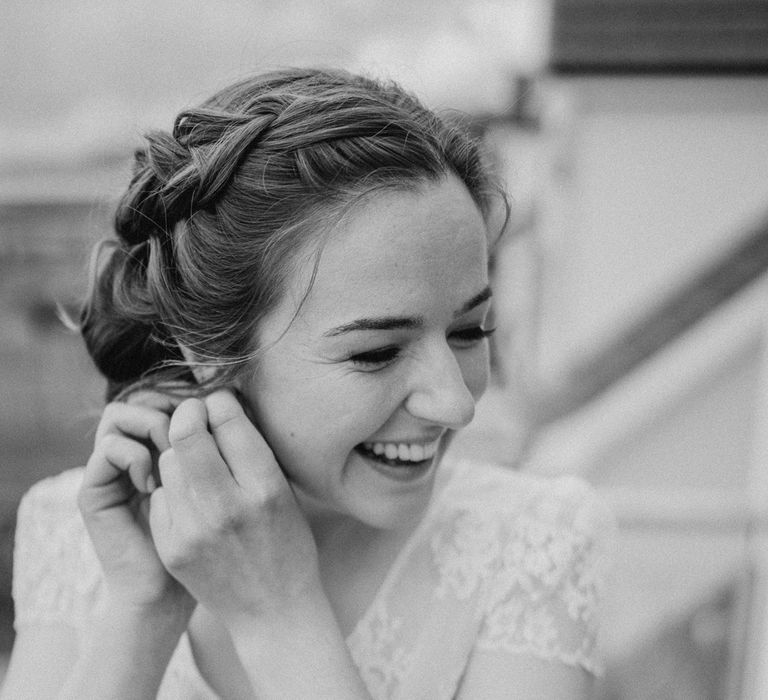 Smiling bride with plaited wedding updo and lace top capped sleeve wedding dress puts in earrings before Dunluce Castle wedding