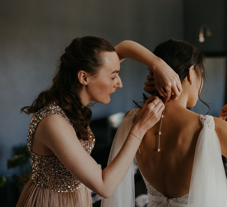 Bridesmaid fastening bride's pearl drop necklace