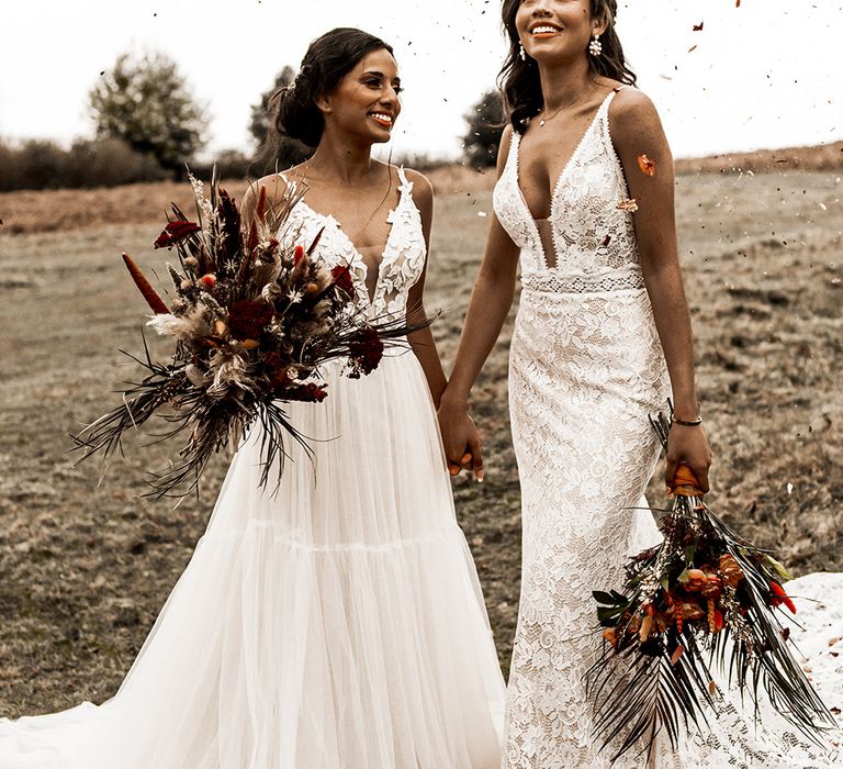 Confetti moment with two brides in a tulle and fitted lace wedding dress holding their orange and red flower bouquet 