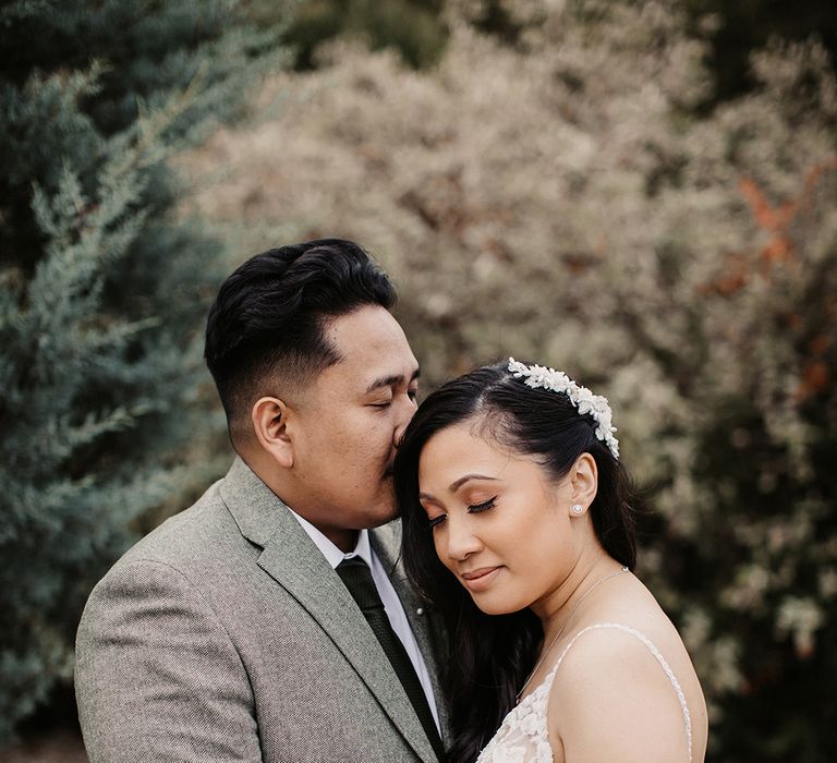 A groom kisses his bride on the forehead for wedding portraits.