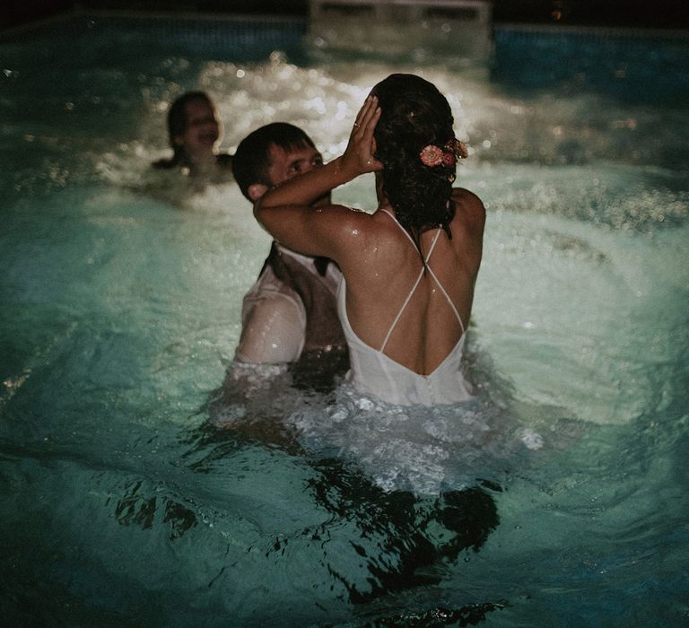 Bride in cross back Rime Arodaky wedding dress in pool with groom in white shirt and light brown waistcoat at garden wedding with burnt orange wedding theme