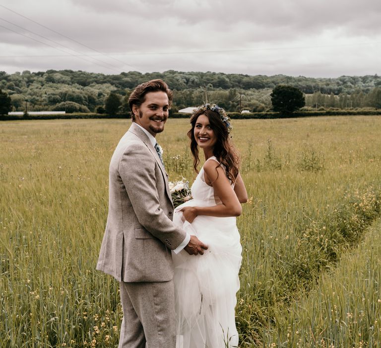 Bride & groom embrace in green fields on the day of their wedding