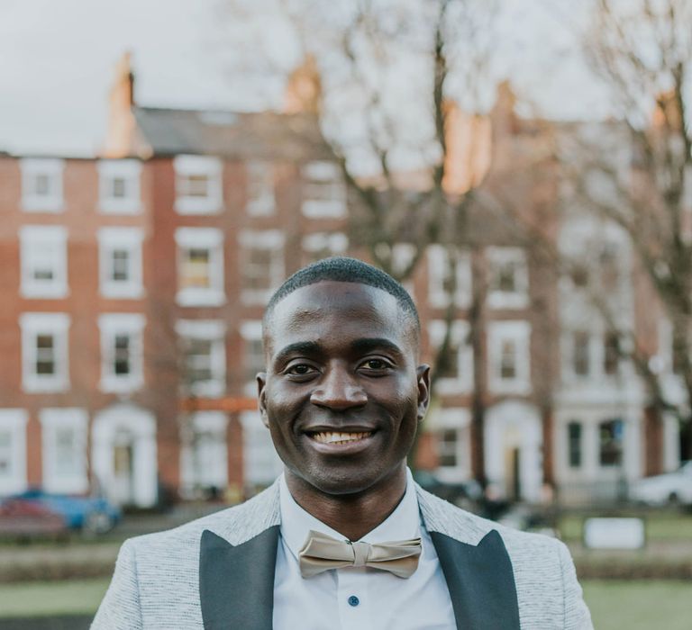 Black groom in a white skirt and bow tie with grey blazer with black lapels 