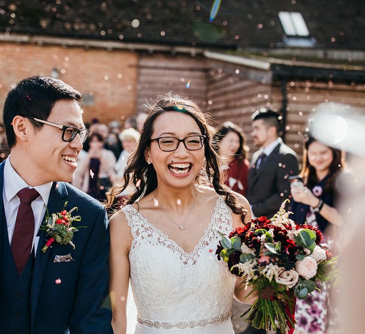 A Chinese couple smile as they walk through confetti shower. They both wear glasses. 