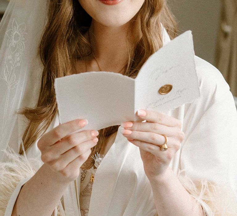 Wedding morning with bride with manicured nails reading a card with long wavy hair, lace veil and gold crown headdress 