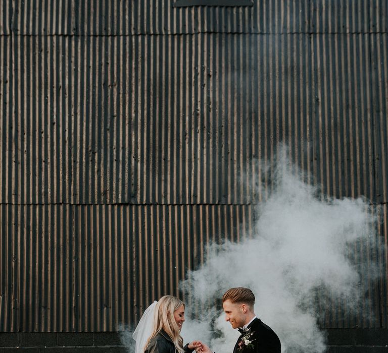 Stylish wedding at Caswell House with bride in a leather jacket and groom in a dinner jacket and a white smoke bomb in the background