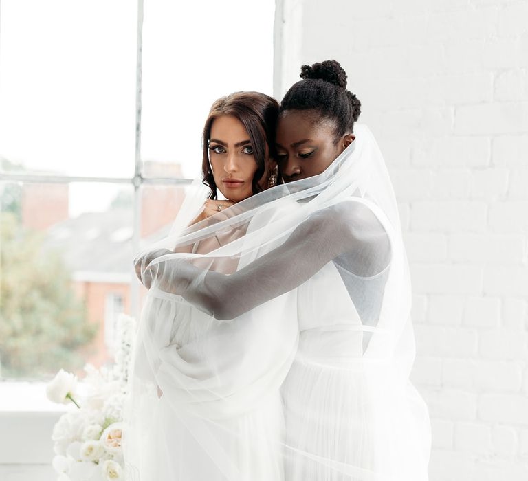 Black bride embracing another bride in a embroidered tulle wedding veil 