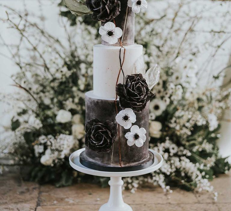 Monochrome wedding cake resting on the intimate reception table decorated with white flowers 