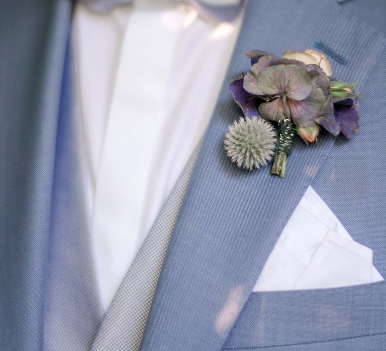 Groom wears dusty blue suit with silver bow-tie and floral buttonhole 