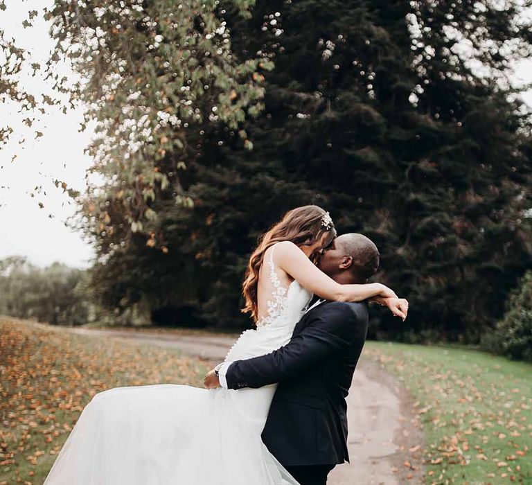 Lace back bridal detailed dress with satin buttons down the back & long curled simple hair kisses Groom in tailored suit outdoors at Cefn Tilla  Court 