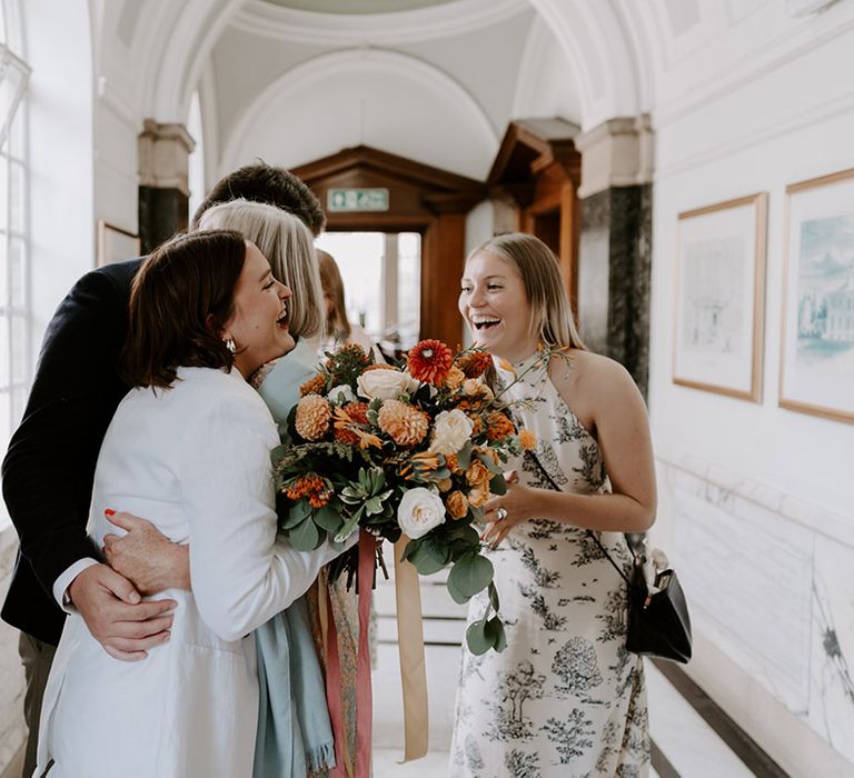 Bride in a suit embracing her guests at intimate town hall ceremony in a trouser suit 