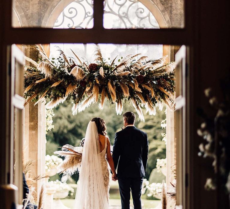 Bride & groom stand with one another under pampas grass installation above