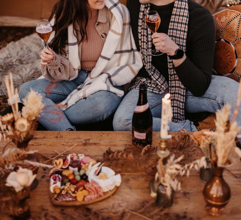 Casual wedding proposal with bride and groom-to-be toasting their engagement at a boho campsite 