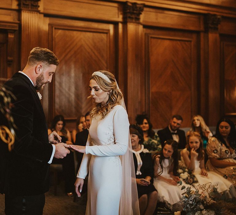 Old Marylebone Town Hall black-tie wedding ceremony with bride in a long sleeve wedding dress and pearl headband and groom in a tuxedo 