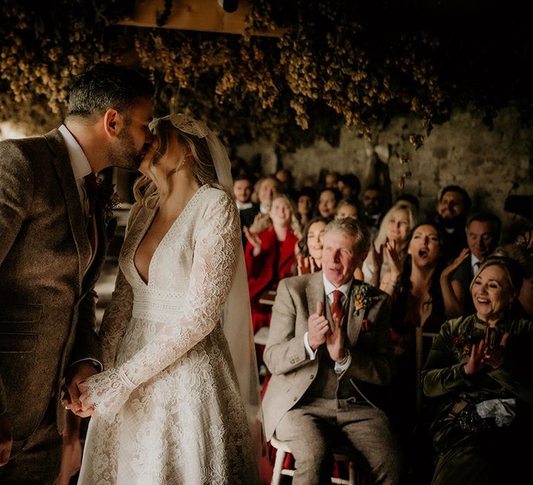 Groom in a wool suit and bride in lace dress kissing at their Lyde court wedding ceremony 