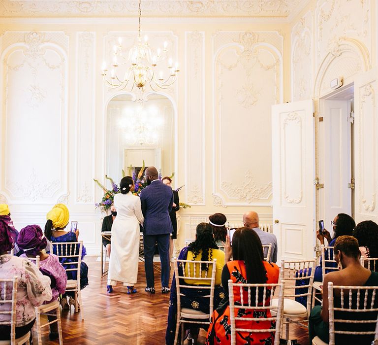 Bride & groom hold hands during wedding ceremony at registry office as bride wears blue wedding shoes