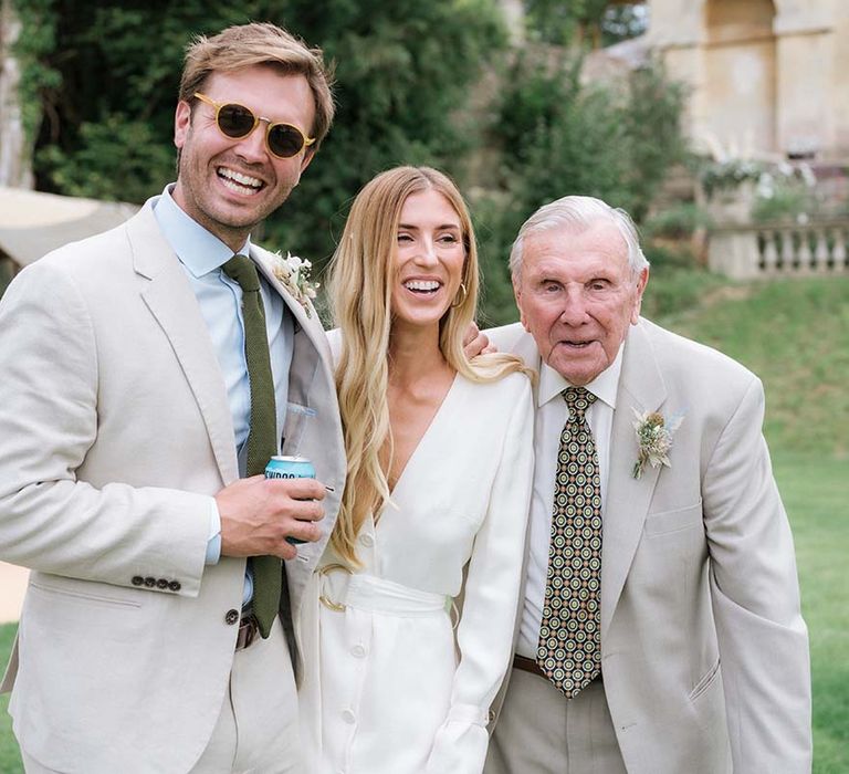 Bride and groom with guest in light coloured suit and green tie to match the colour scheme and dried flower buttonholes 