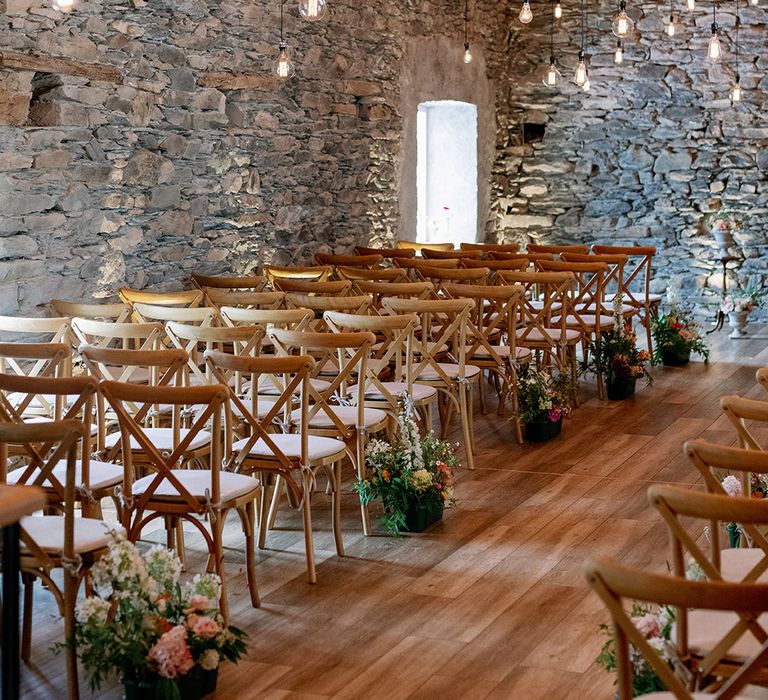 Wedding venue with hanging exposed lightbulbs and pink wooden chairs for guests with simple flower aisle decoration