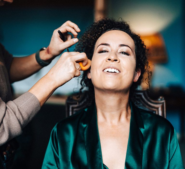 Bride in satin green robe gets her makeup done for her wedding day 