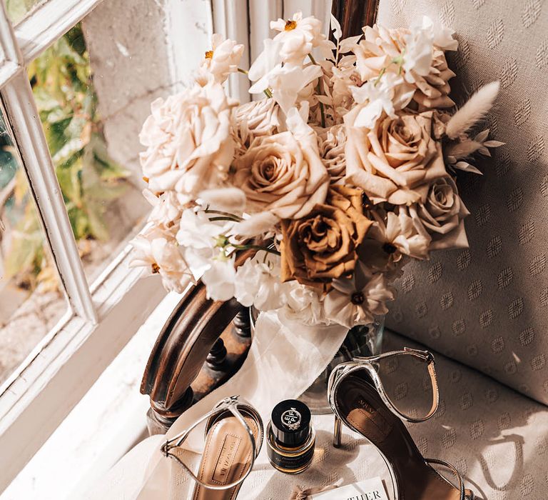 Silver wedding shoes with bride's perfume and ring with wedding bouquet of toffee roses, and other beige, rust and white flowers