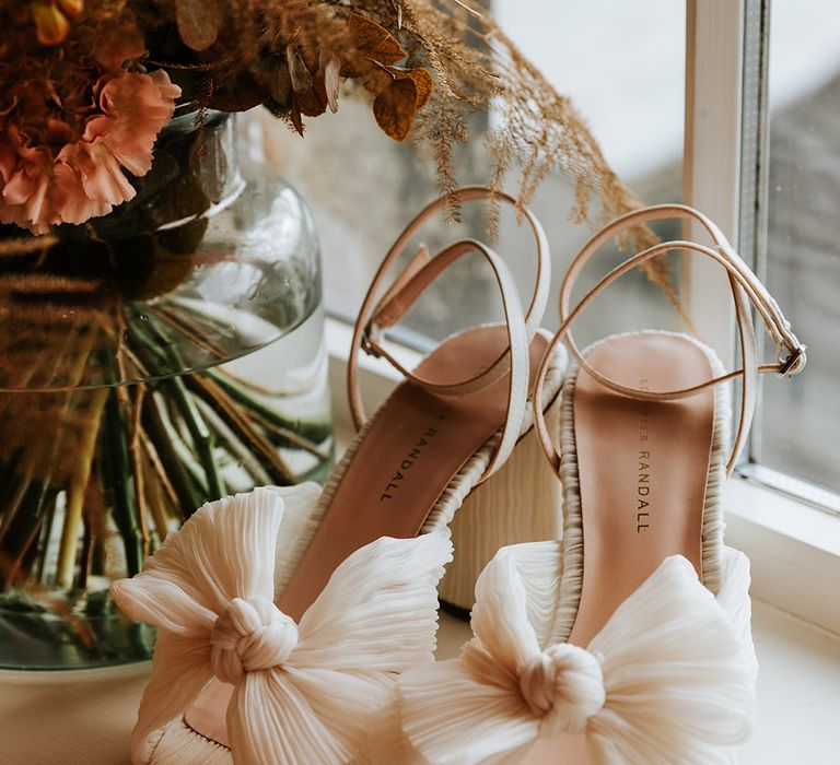 Loeffler Randall white bow wedding shoes next to vase of autumnal flowers 