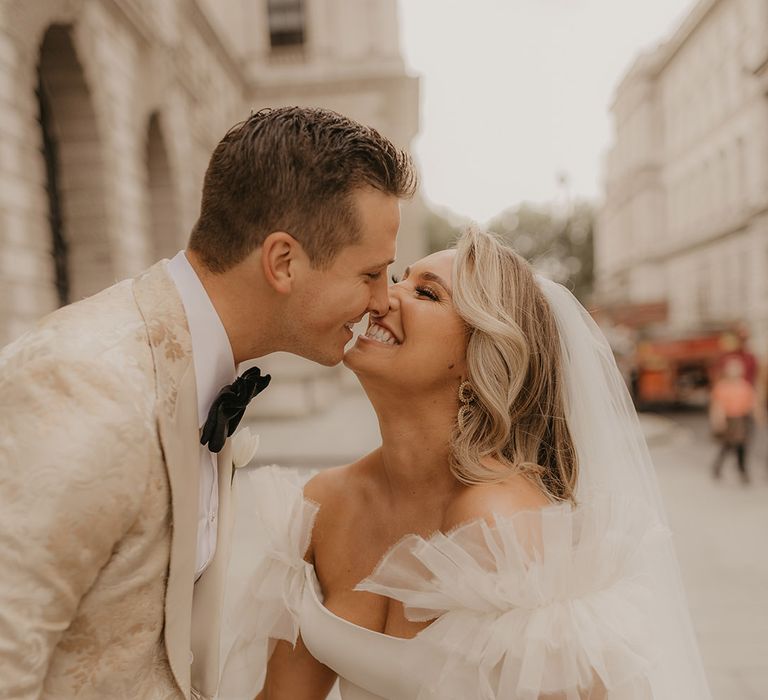 Bride in ruffle wedding dress smiles brightly at groom who holds her hand in gold custom tuxedo