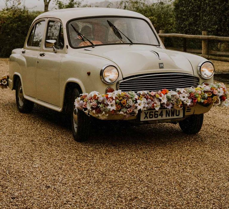 Cream classic wedding car with floral arrangement on bonnet