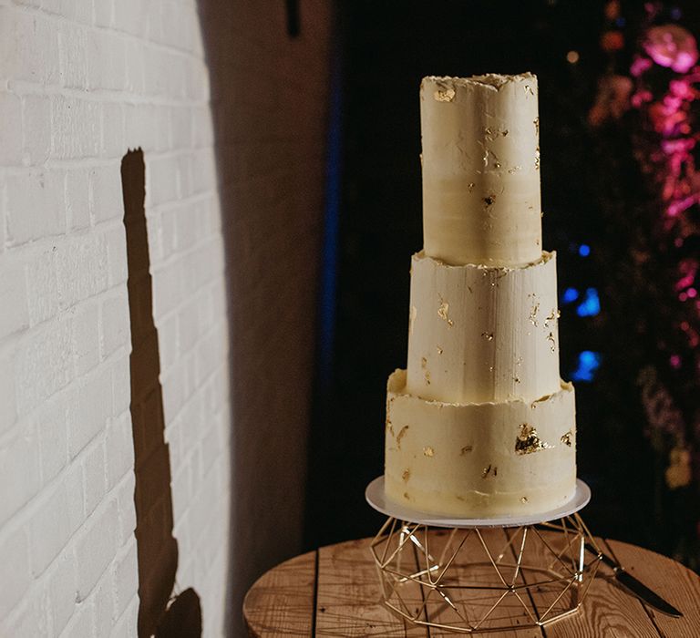 Three tier tall wedding cake frosted with buttercream and gold flakes