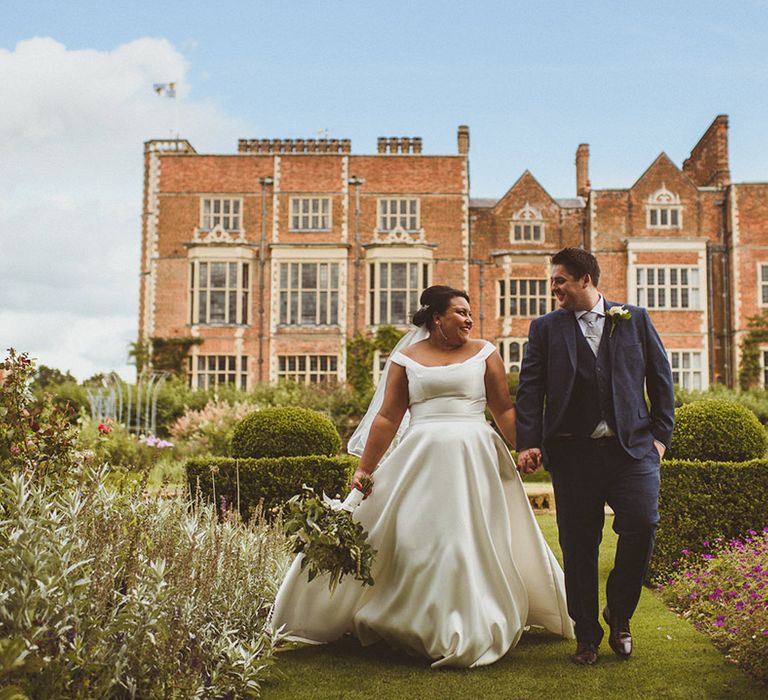 Bride and groom walk in the gardens in front of Hatfield House country house wedding venue 