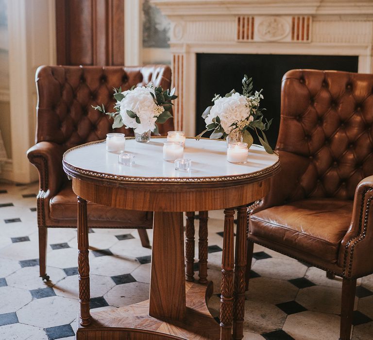 Candles and glass vase of white flowers with dark brown leather chairs 