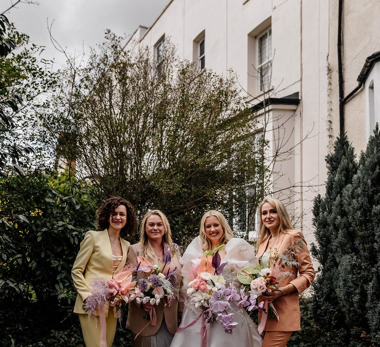 Bridal party in different coloured bridesmaid suits with the bride in a JESUS PEIRO wedding dress holding a tropical flower bouquet with orchids, anthuriums and astilbe 