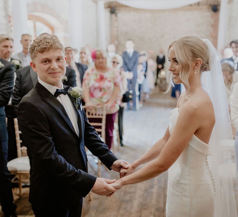 Groom smiles at the camera as he holds the bride's hands during the wedding ceremony 