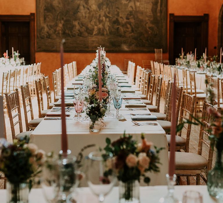 White tablecloths across banquet tables finished with small pastel floral bouquets and pink pillar candles 