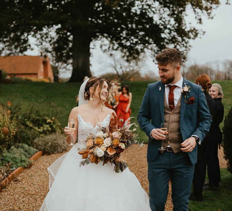 Bride and groom walk together after their wedding ceremony carrying a glass of Champagne 