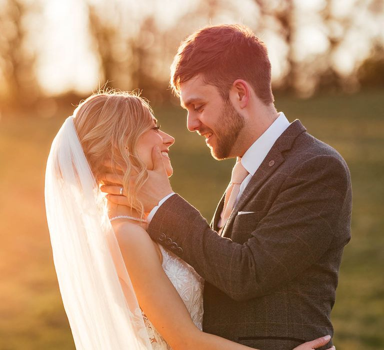 Bride and groom smile and embrace each other during golden hour 