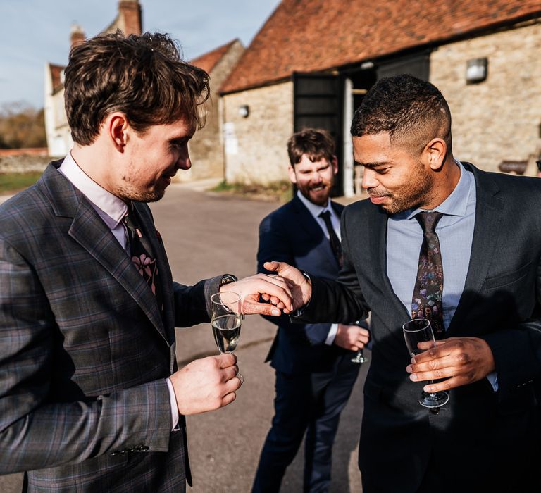 Groom wears tartan suit with floral tie and stands with wedding guest who looks at his wedding ring 