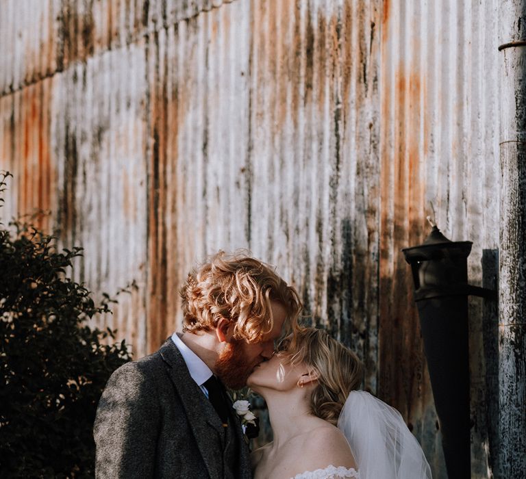 Bride in a lace long sleeve wedding dress kisses with the groom in a grey woollen suit 