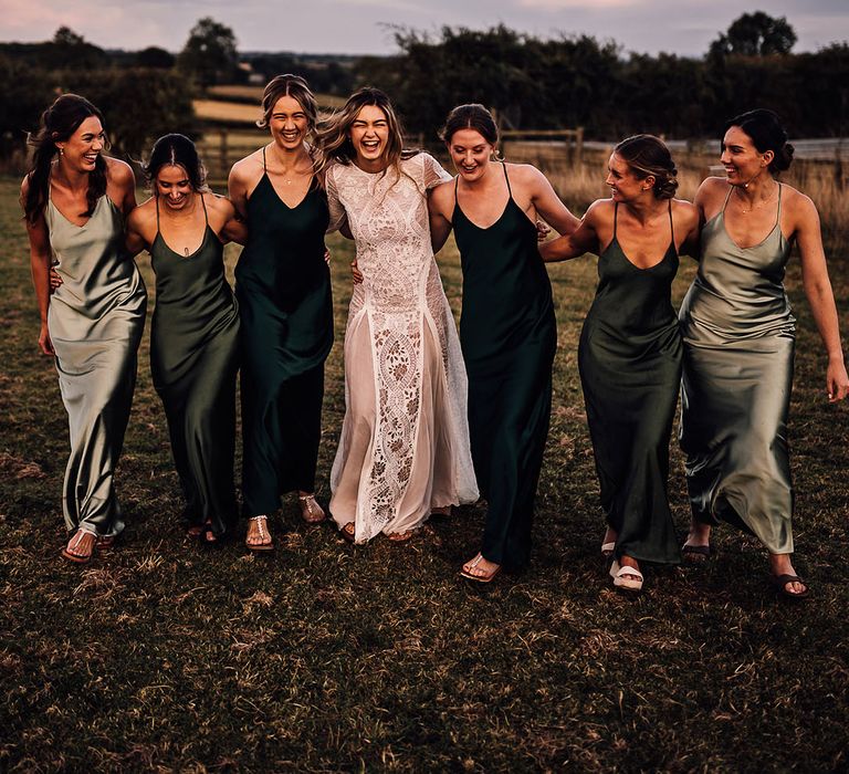 Bridesmaids in green dresses with different shades standing with the bride in a lace boho wedding dress