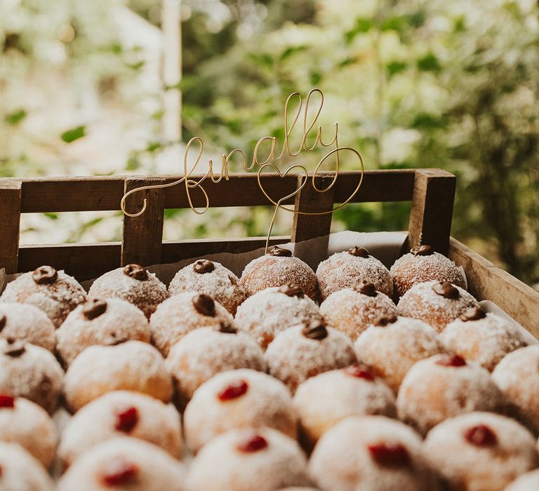 Filled doughnuts for the wedding favours with a wire cake topper saying 'finally' in a wooden crate box 