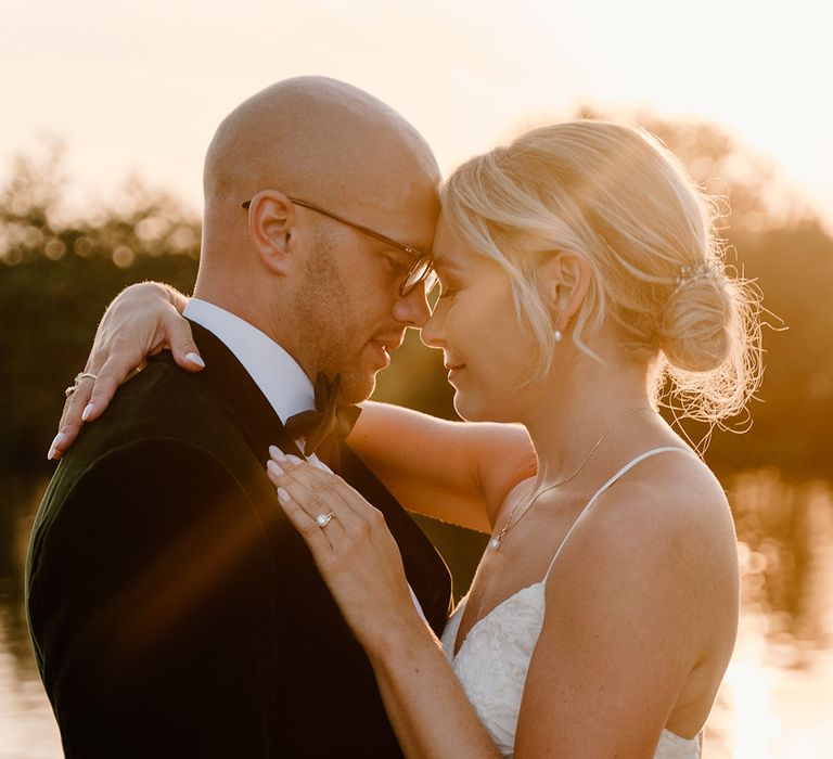 Bride wears her blonde hair in low up-do and embraces her groom during golden hour