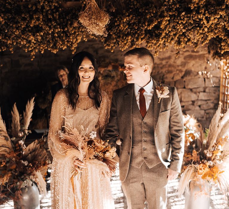 Bride & groom stand on Moroccan styled rug surrounded by dried floral installations at Lyde Court