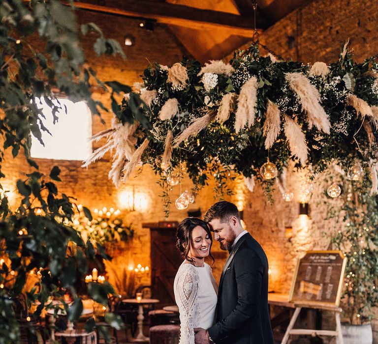 The bride and groom share an intimate moment under the pampas grass and foliage cloud with winter baubles 