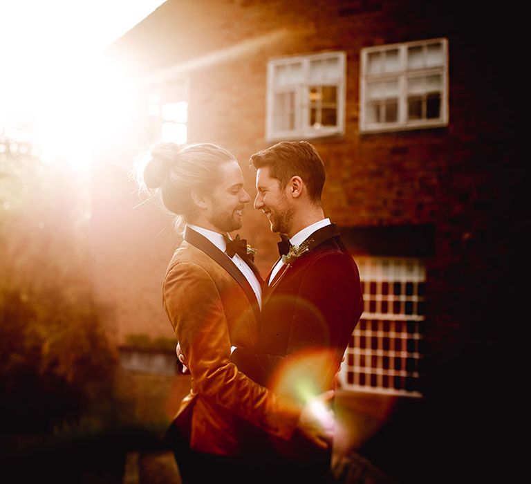 Grooms stand outdoors during golden hour portraits on their wedding day 