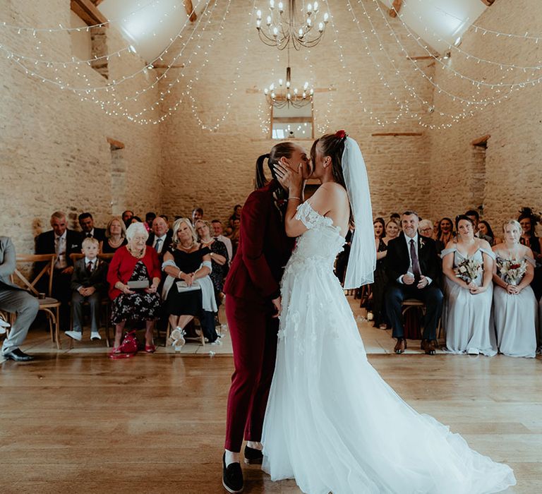 Brides share their first kiss as a married couple at their rustic barn wedding 