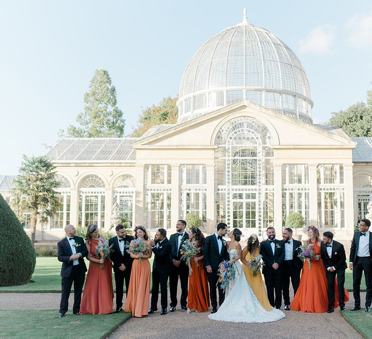 Bride & groom stand with their wedding party outside Syon Park Conservatory 