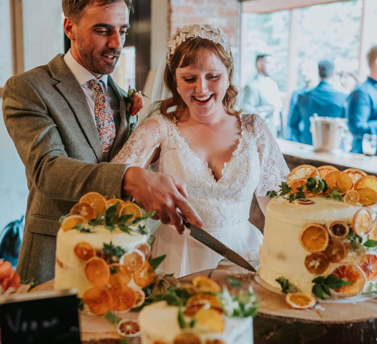 The bride and groom cut one of their frosted vegan wedding cakes decorated with dried orange slices 