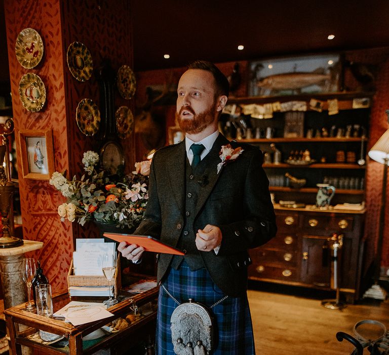 Best man wearing dark grey blazer and waistcoat, blue tie, autumnal boutonniere and dark blue kilt doing wedding speech