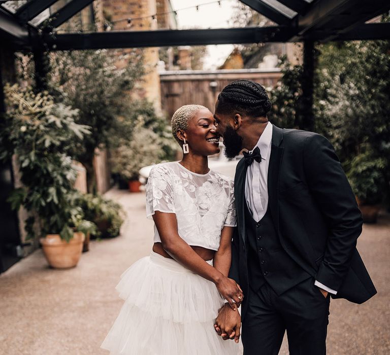 Bride and Groom holding hands in a black wedding suit and a bridal two piece set featuring embroidered floral top and layered skirt