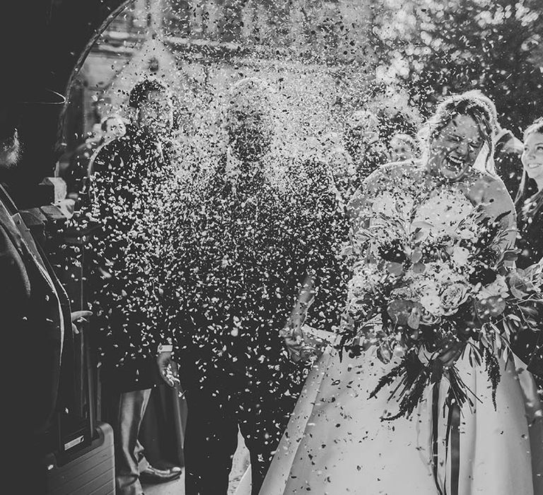 Black and White wedding photography showing Bride and Groom laughing through a confetti shot