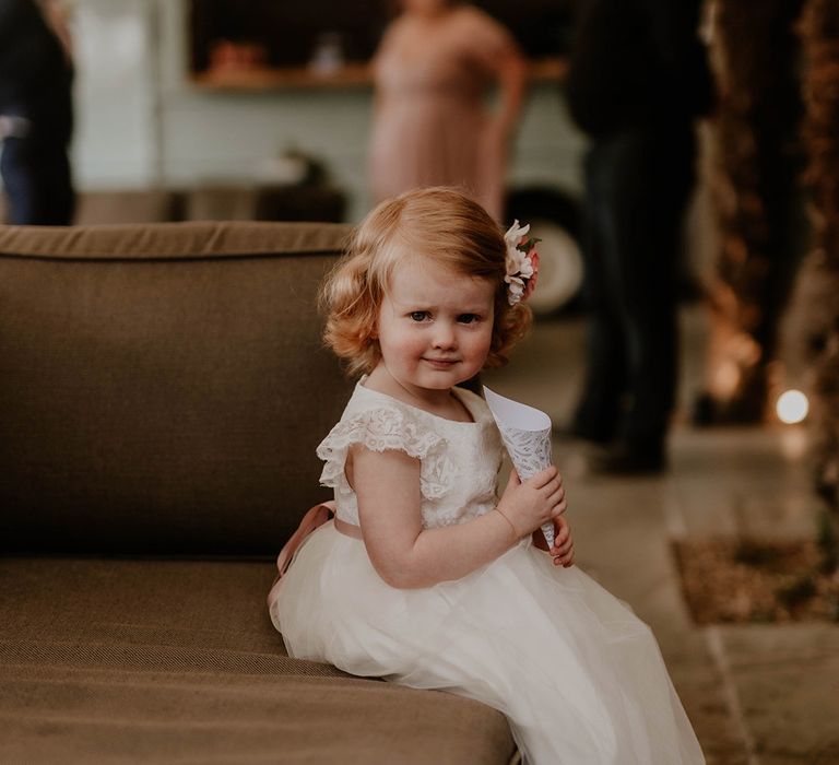 Flower girl wears white floor length dress complete with scallop lace arm and pale pink belt 